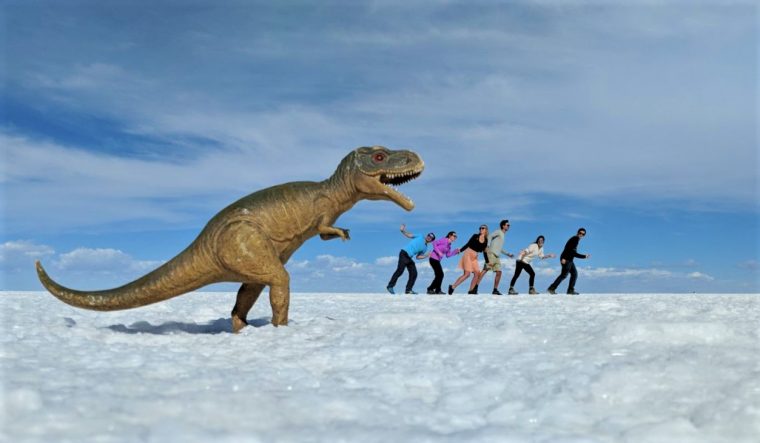 A photo of a plastic dinosaur apparently chasing six people on ice flats, created using perspective.