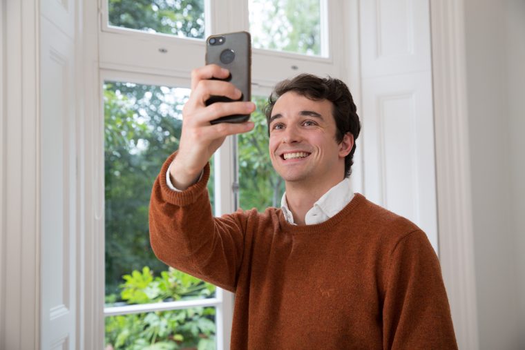 man taking a selfie/video call from above in front of a window